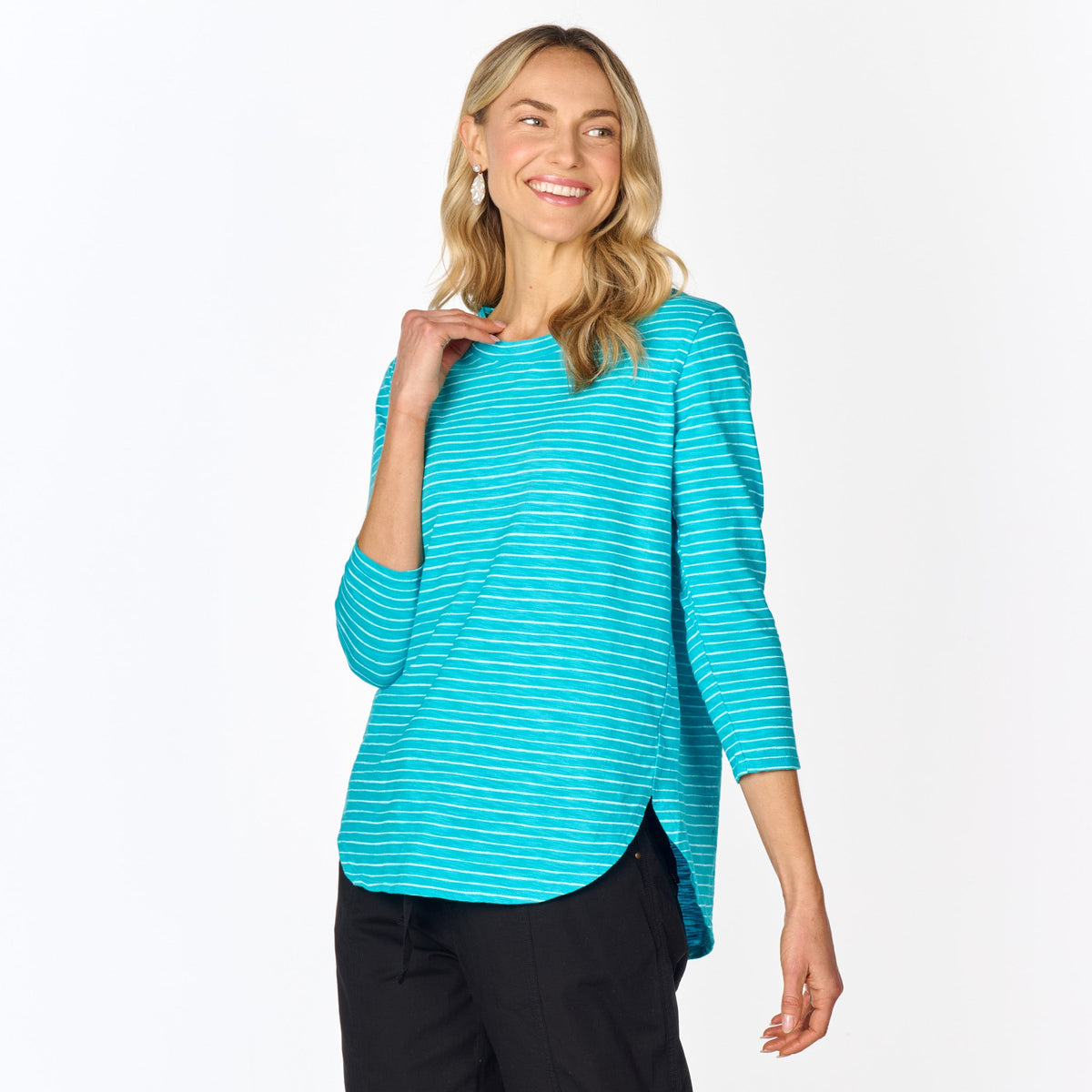 A woman with long blonde hair is wearing the Fresh Produce Clothes Ocean Stripe Catalina Top (Clearance) paired with black pants, smiling and looking to the side against a plain white background.